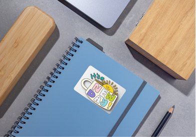 Blue notebook with a colorful sticker on a gray surface with wooden blocks and a pencil.